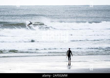 Surfer catching a wave while another surfer walks out of water Stock Photo