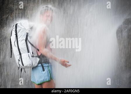 Laughing woman standing under waterfall Stock Photo