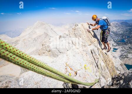 Man rock climbing on high ridgeline above valley Stock Photo