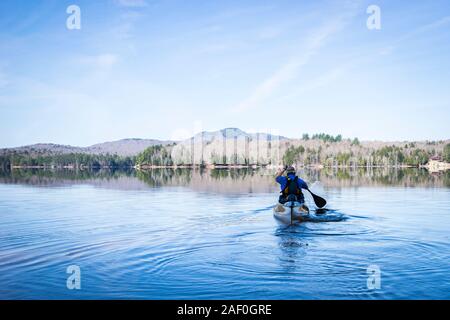 Man paddling canoe on calm water under blue sky Stock Photo