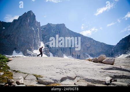 Man walking through the mountains with big cliffs behind Stock Photo