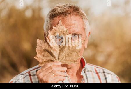 The senior man looking through the heart-shaped hole in the maple leaf. Autumn concept. Selective focus Stock Photo