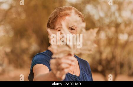 Eye of mature woman seen through a heart-shaped leaf,blue blouse Stock Photo