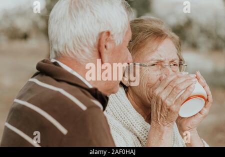 Older woman drinking coffee while her husband looks at her Stock Photo