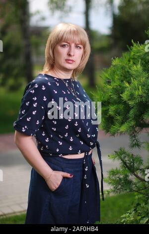 Blonde woman standing near green bush Stock Photo