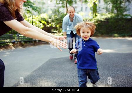 Boy running towards camera as parents playfully chase him Stock Photo