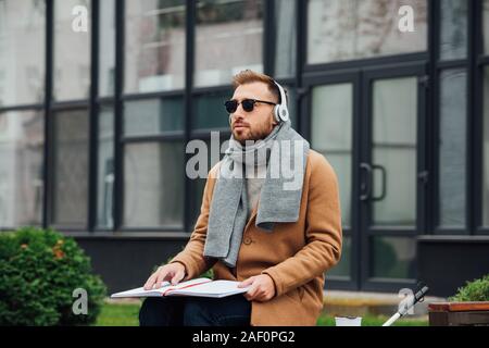 Blind man in headphones reading book on bench in park Stock Photo