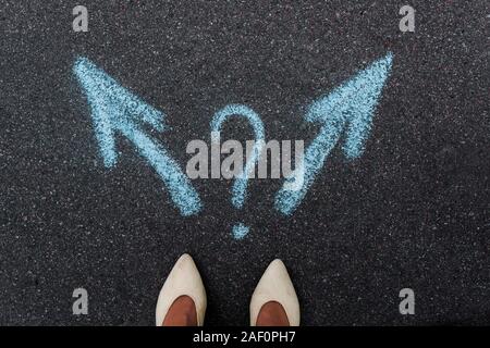 top view of woman standing near blue directional arrows and question mark on asphalt Stock Photo