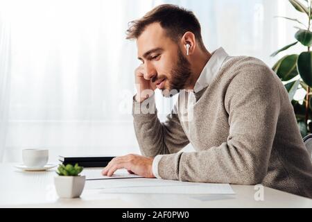 Side view of blind man reading and using wireless earphones at table Stock Photo