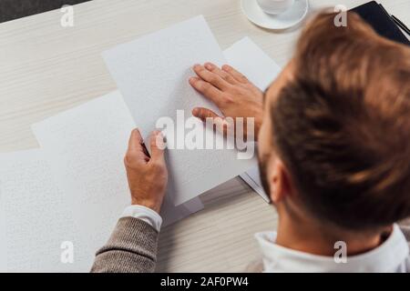 Overhead view of blind man reading braille font from paper at table Stock Photo