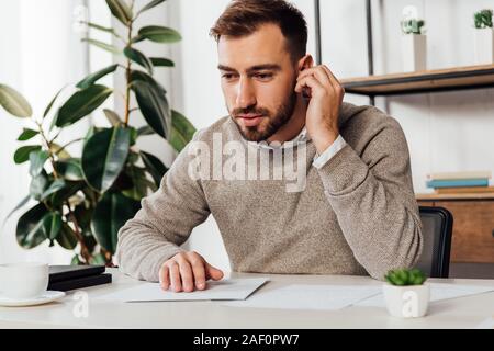 Blind man using wireless earphones while reading at table Stock Photo