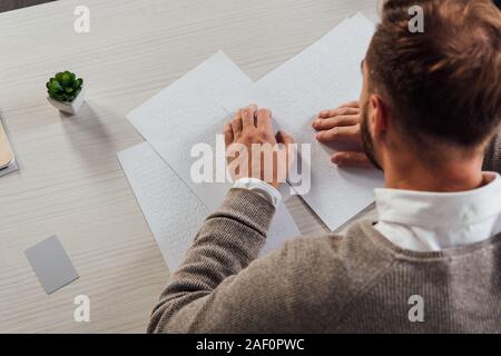 Overhead view of blind man reading braille font beside card with copy space on table Stock Photo