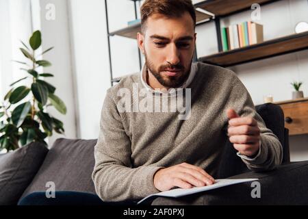 Visually impaired man reading braille font on sofa in living room Stock Photo