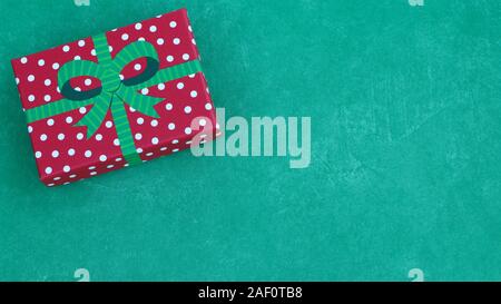 top view of wrapped red and white polka dot gift box with a green bow on a festive green background with copy space Stock Photo