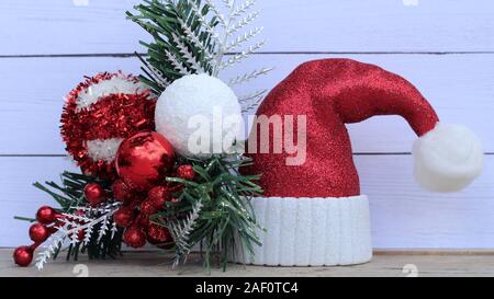 red and white Santa hat standing on a white wood background next to christmas bulbs and a pine branch with writing space Stock Photo