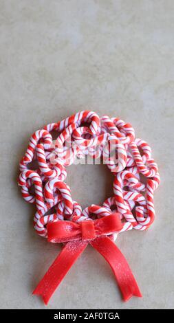 red and white candy cane wreath with a red bow laying flat on a tan color background with writing spa Stock Photo