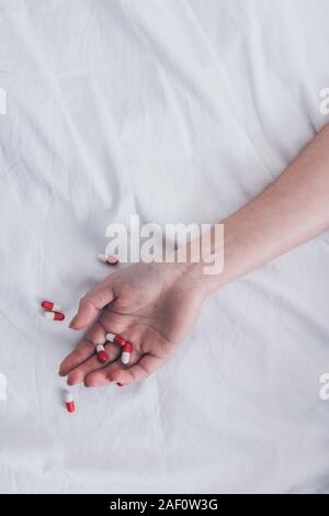 cropped view of female hand with pills on white bedding Stock Photo