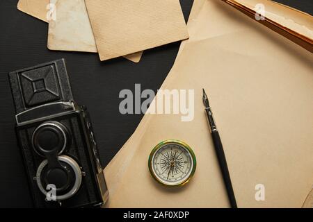 top view of vintage camera, paper, fountain pen, compass on black background Stock Photo