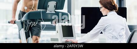 panoramic shot of sportsman running on treadmill near doctor during endurance test in gym Stock Photo