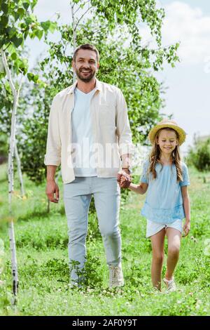 happy father and daughter standing near green plants and holding hands Stock Photo