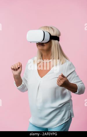 senior woman wearing virtual reality headset and gesturing isolated on pink Stock Photo