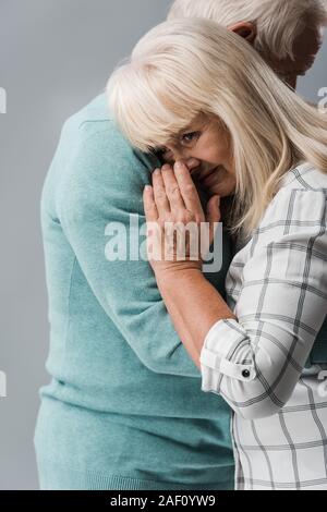 cropped view of husband hugging retired wife covering face while crying isolated on grey Stock Photo