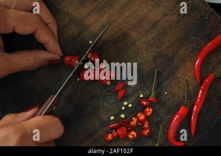 Woman slices the red chili pepper on the wooden board Stock Photo