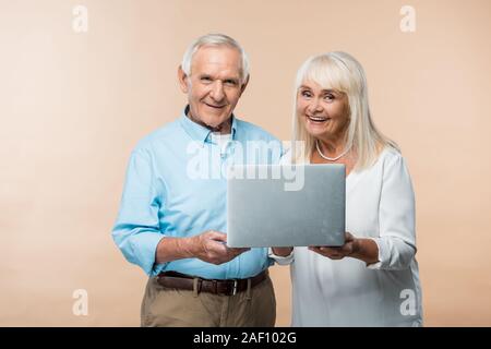 happy retired couple using laptop and smiling isolated on beige Stock Photo