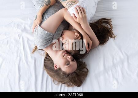 top view of two smiling lesbians embracing while lying on bed Stock Photo