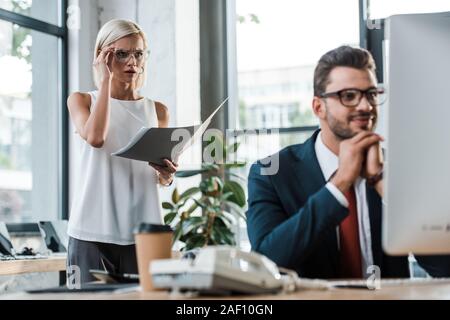 selective focus of surprised businesswoman looking at computer monitor near handsome man Stock Photo