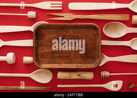 top view of empty rectangular wooden dish on red background with kitchenware Stock Photo