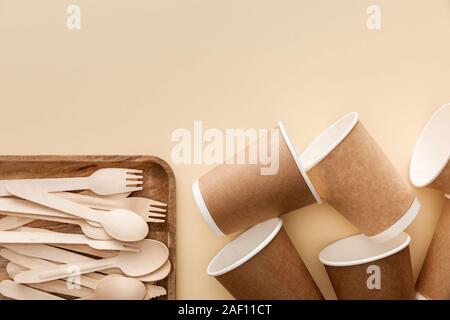 top view of rectangular wooden dish with forks and spoons near paper cups on beige background Stock Photo