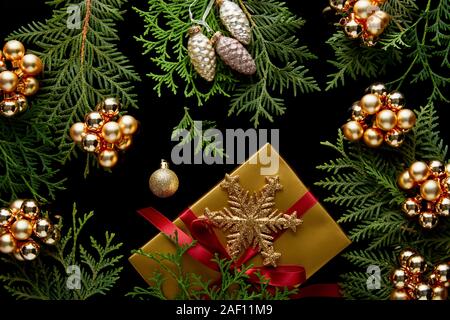 top view of shiny golden Christmas decoration, green thuja branches and gift box isolated on black Stock Photo