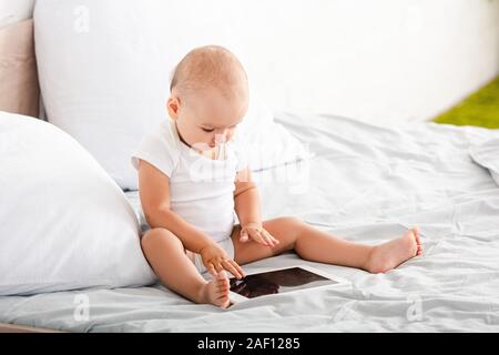 Cute barefoot child in white clothes pointing with fingers at digital tablet Stock Photo