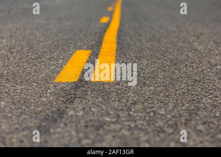 low angle closeup view of yellow dividing and no passing lines and stripes in middle of asphalt road Stock Photo