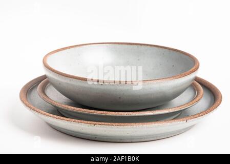 A set of stoneware dinner service with different plates and bowls on a white plain background. Stock Photo