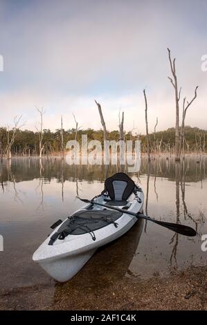 Single beached kayak and paddle on the shoreline at sunrise at Lake Tinaroo, Queensland, Australia. Stock Photo