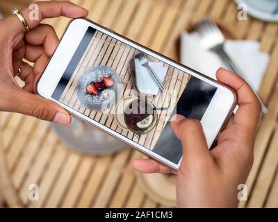 Woman's hand taking a photo of delicious chocolate tart on ceramic dish by smartphone in cafe. Smartphone food photography trendy concept. Stock Photo