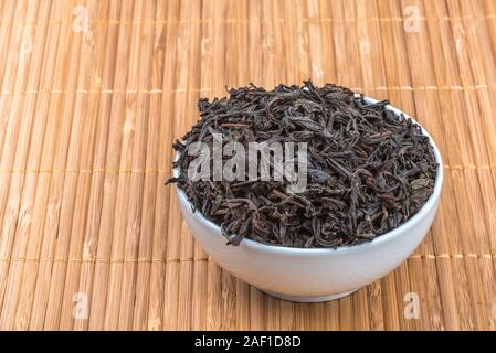 Dried tea is poured into a ceramic cup on a bamboo mat Stock Photo