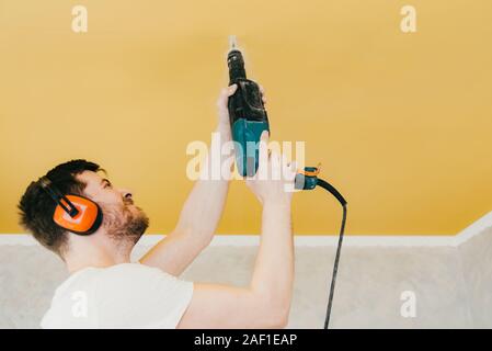 the guy is drilling a hole in the ceiling with a drill in his apartment Stock Photo