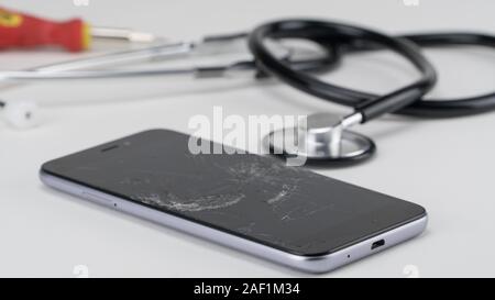Diagnosing the phone with a stethoscope, near a screwdriver. Phone repair concept Stock Photo