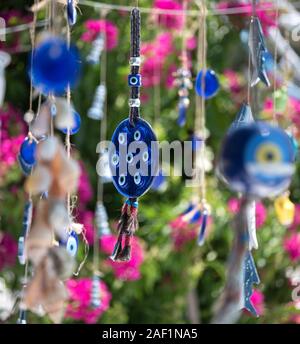 Evil eye charms, trukish souvenirs hanging  agianst a background of mediterranean flowers. Turkish Aegean Coast, Turkey Stock Photo