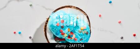 top view of delicious blue ice cream with sprinkles on coconut half on marble grey background, panoramic shot Stock Photo