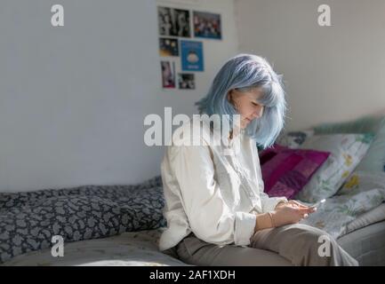 Young woman using cell phone in bedroom Stock Photo