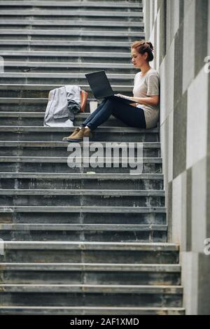 Young woman concentrated on work sitting on steps with laptop Stock Photo