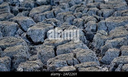 Severe drought conditions cause deep, gaping cracks in the dry bed of a parched creek. A stark reminder of extreme climate and water scarcity. Stock Photo
