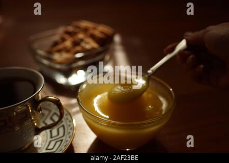 Tea time. Honey in a glass bowl with a spoon, a cup of tea on a saucer, cookies in a vase on the table. Stock Photo
