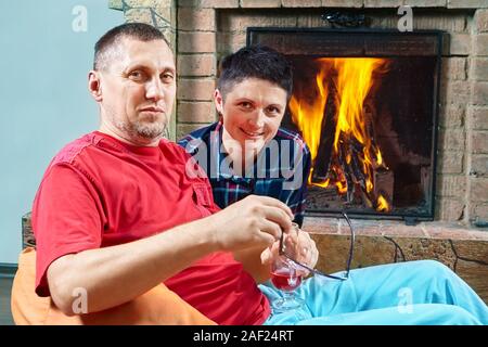 Mature husband and wife are sitting on the bean bag chairs near fireplace and posing to hte camera, they are smiling and looking straight on. Stock Photo