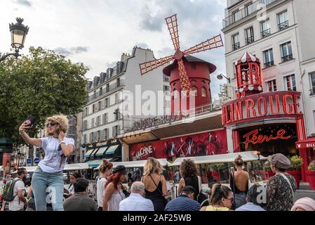 Paris (France): atmosphere in the district of Montmartre, tourists taking pictures in front of the Moulin Rouge cabaret. Young woman taking a selfie Stock Photo
