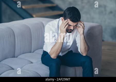 Portrait of his he nice attractive serious bearded guy sitting on divan touching temples suffering from headache at modern industrial loft interior Stock Photo
